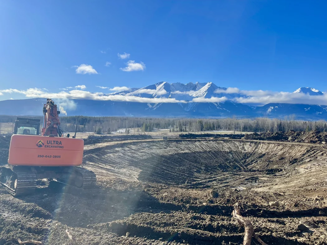 Ultra Excavating excavator beside a freshly opened basin with the Bulkley Range behind it