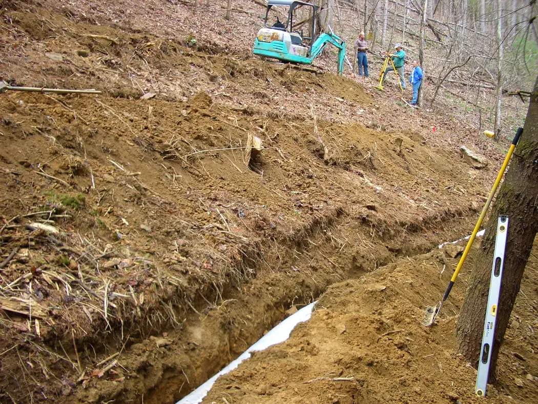 Open trench cut down a wooded slope with bedded pipe ready for a septic and sewer system
