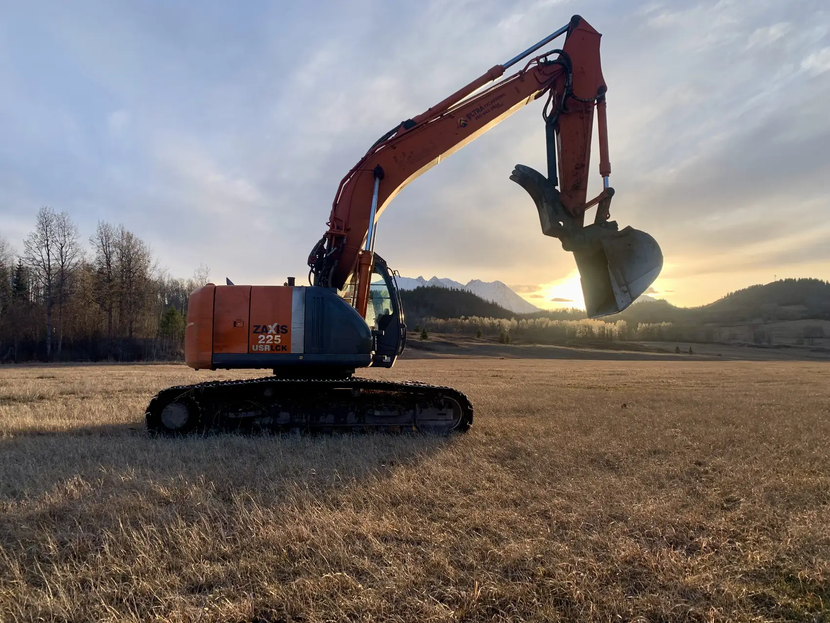 Ultra Excavating tracked excavator parked in a Bulkley Valley field at sunset